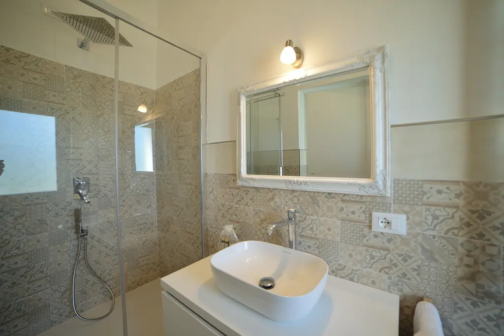 Bagno moderno con piastrelle decorate, doccia a vetro e specchio con cornice bianca